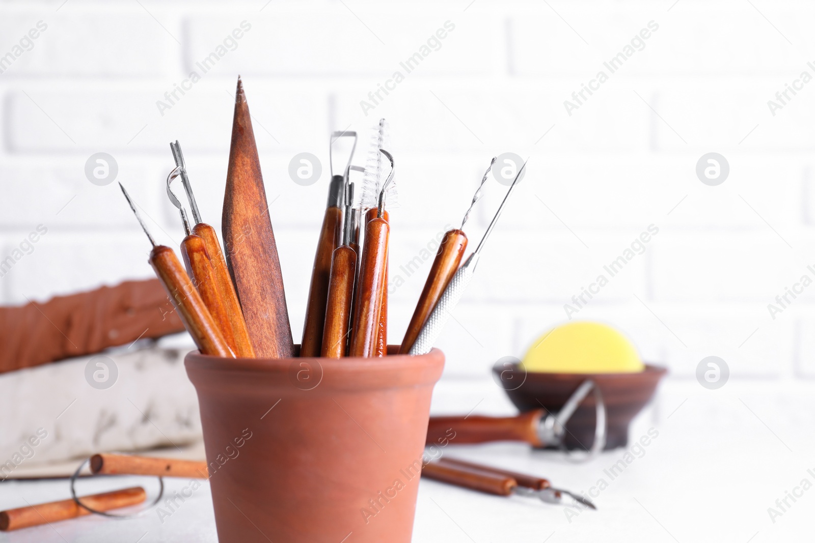 Photo of Clay and set of crafting tools on white table against brick wall, closeup