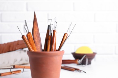 Photo of Clay and set of crafting tools on white table against brick wall, closeup