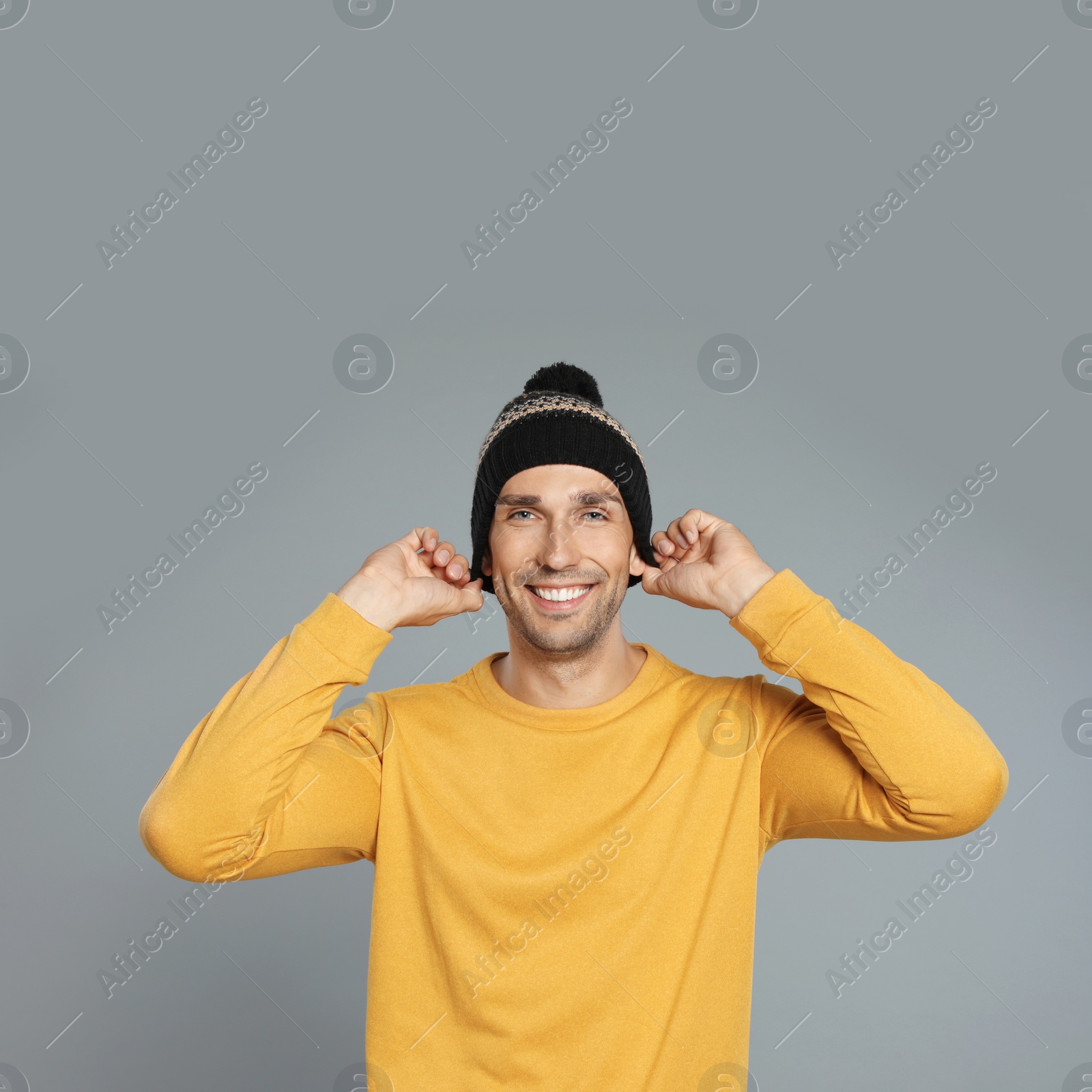 Photo of Happy young man in hat and yellow sweatshirt on grey background. Winter season