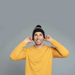 Photo of Happy young man in hat and yellow sweatshirt on grey background. Winter season