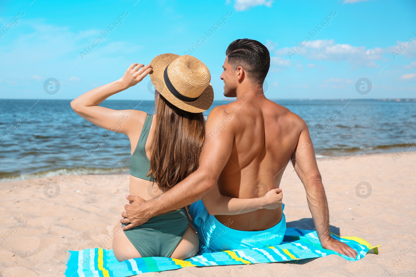 Photo of Woman in bikini and her boyfriend sunbathing on beach, back view. Lovely couple