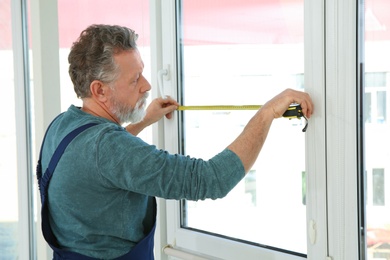 Service man measuring window for installation indoors