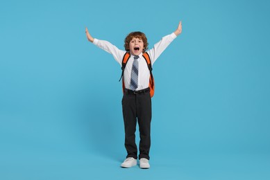 Emotional schoolboy with backpack on light blue background