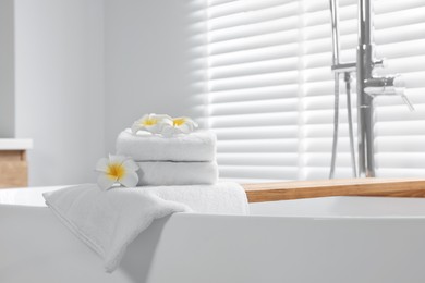 Photo of Fresh white towels and plumeria flowers on tub in bathroom. Space for text