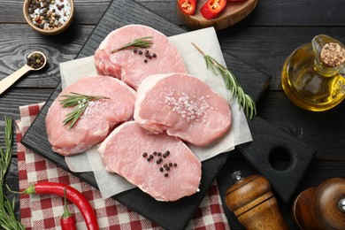 Pieces of raw pork meat and spices on black wooden table, flat lay