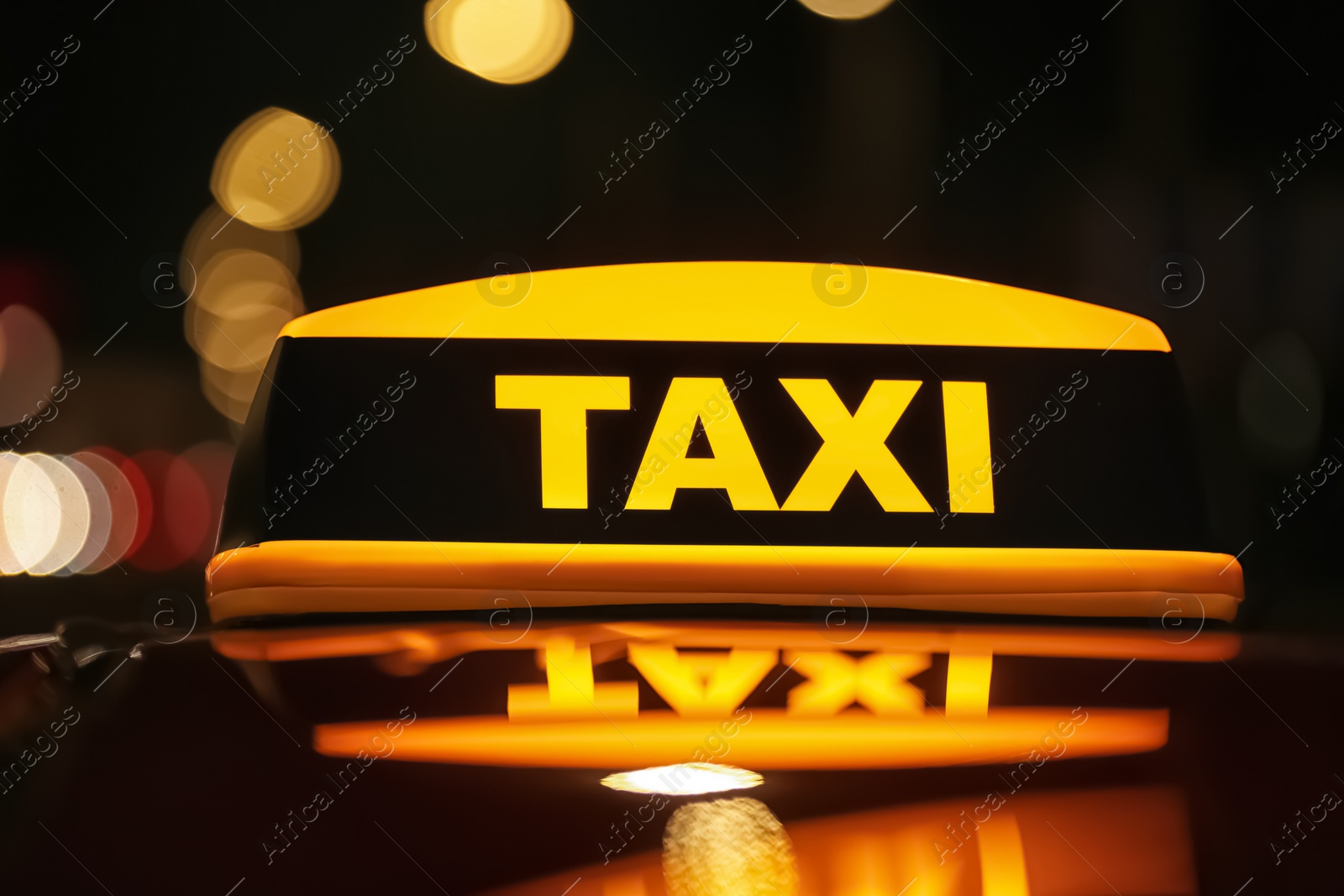 Photo of Taxi car with yellow roof sign on city street at night, closeup