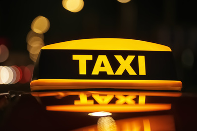 Photo of Taxi car with yellow roof sign on city street at night, closeup