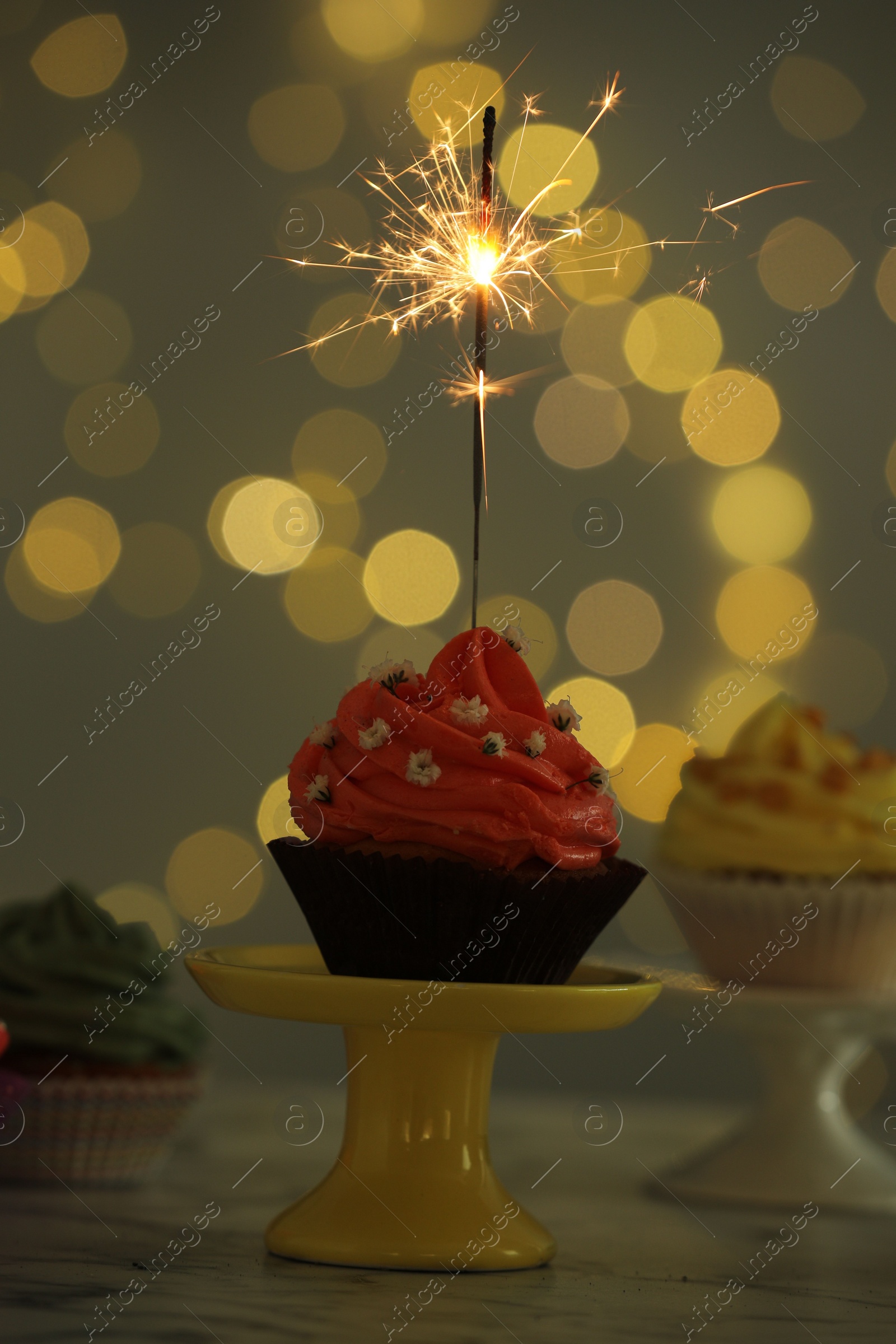 Photo of Delicious cupcake with sparkler on table against blurred lights