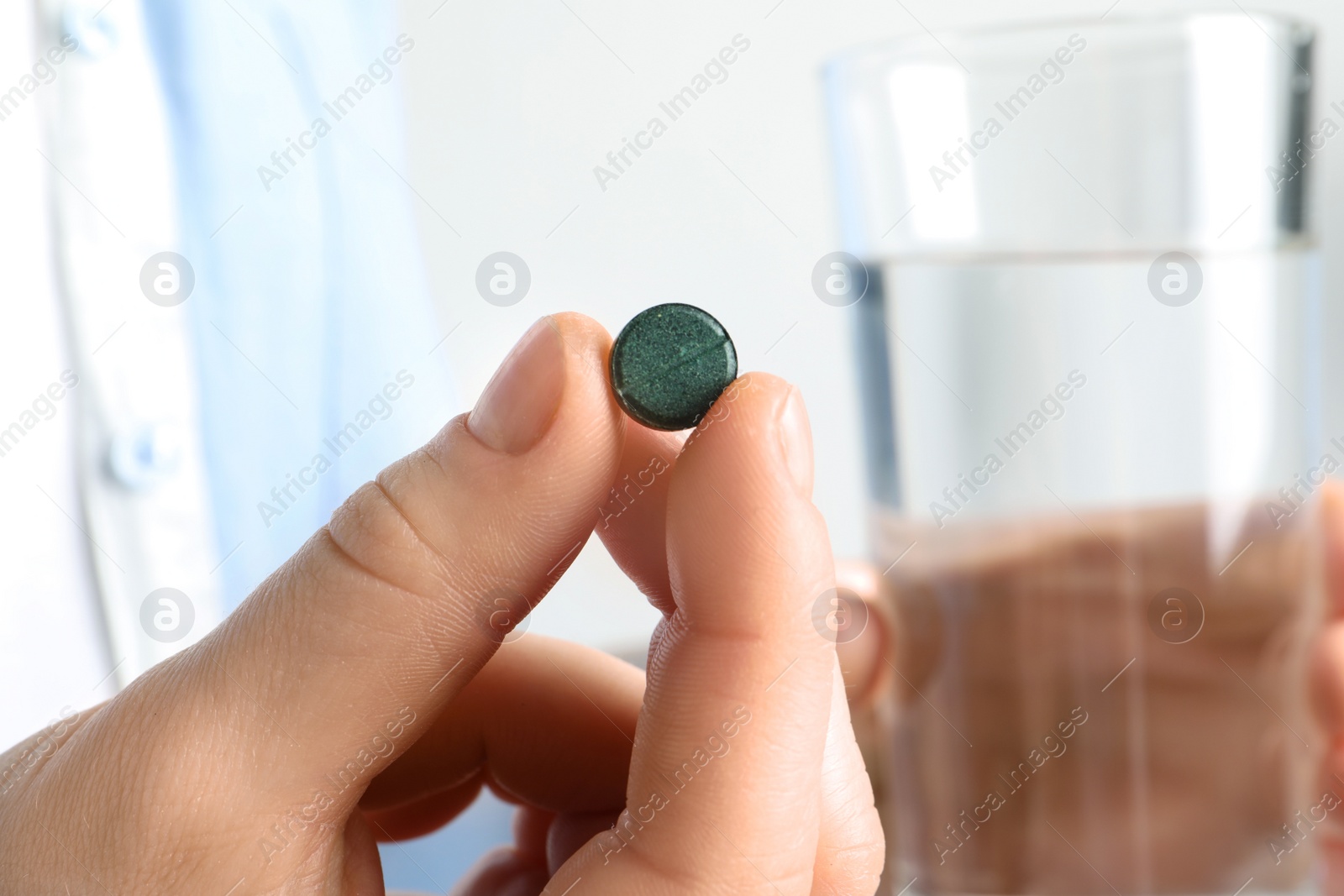 Photo of Woman holding spirulina pill and glass of water, closeup