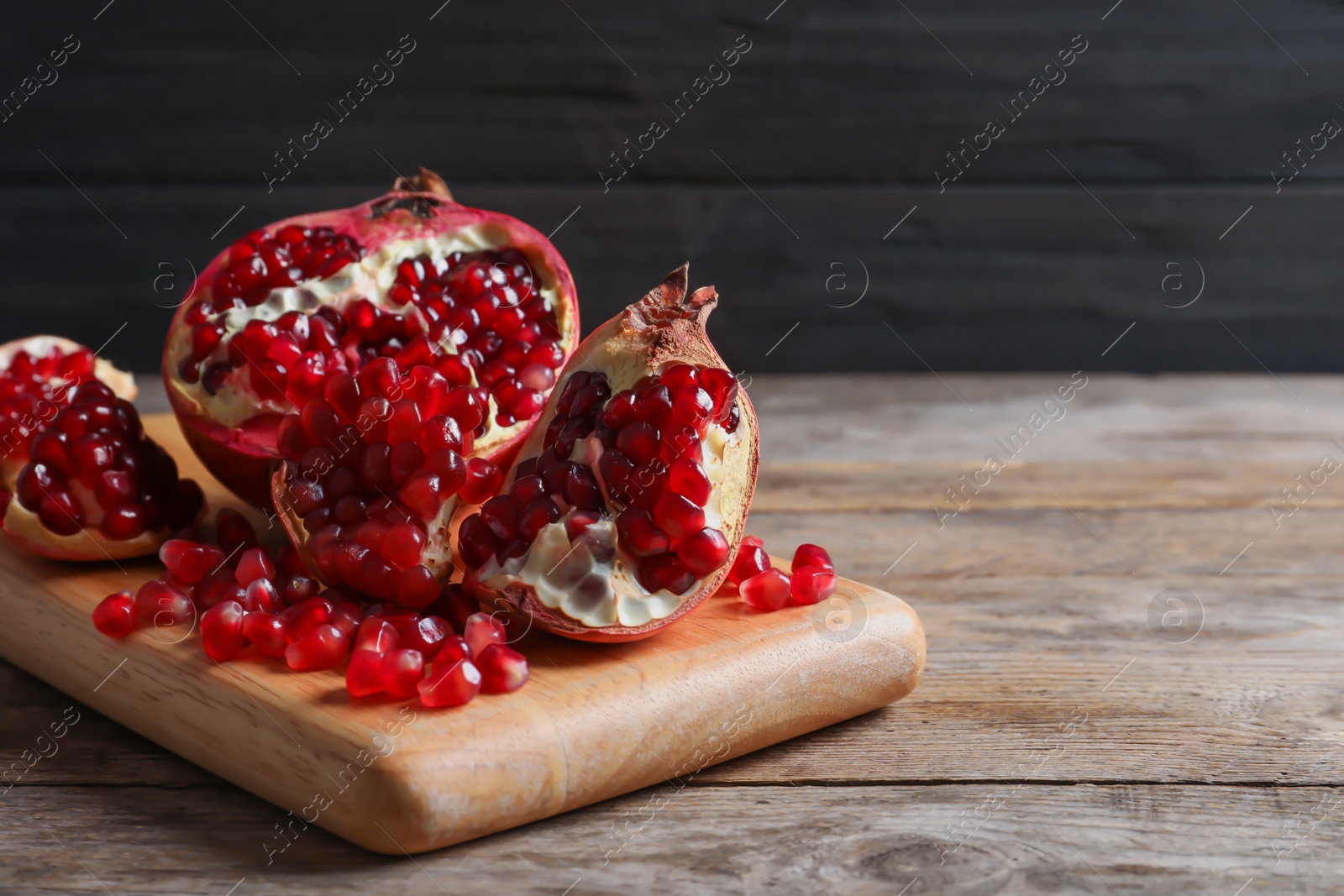 Photo of Board with ripe pomegranates and seeds on wooden table, space for text