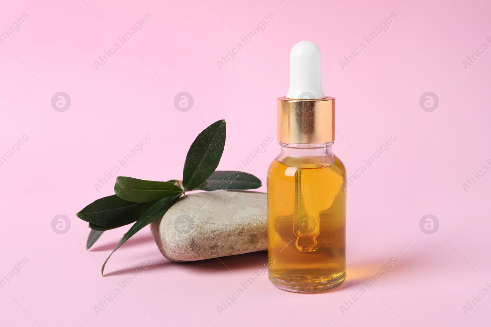 Photo of Bottle with cosmetic oil, green leaves and stone on pink background. Space for text