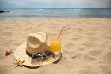 Photo of Straw hat, sunglasses and refreshing drink on sandy beach near sea. Space for text