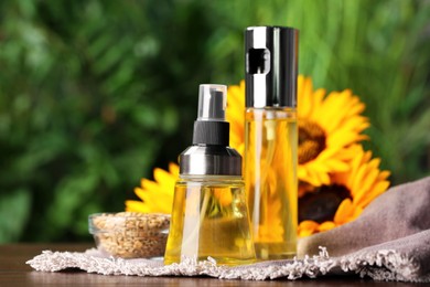 Photo of Spray bottles with cooking oil near sunflower seeds and flowers on wooden table against blurred green background