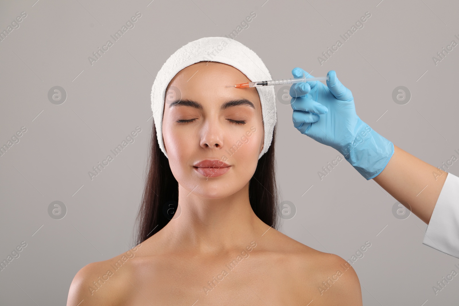 Photo of Doctor giving facial injection to young woman on light grey background. Cosmetic surgery