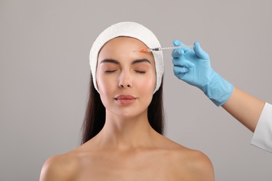 Doctor giving facial injection to young woman on light grey background. Cosmetic surgery