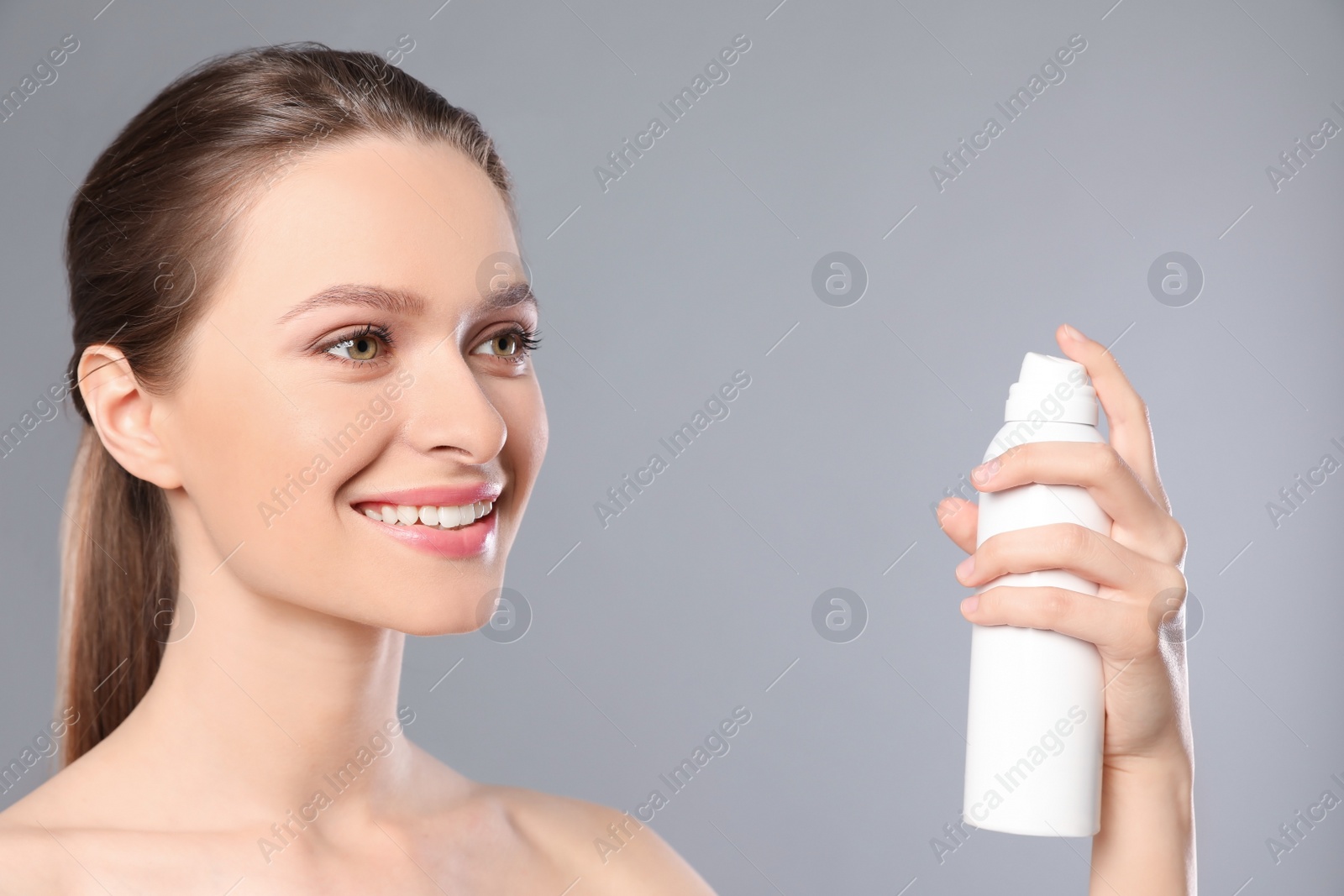 Photo of Young woman with bottle of thermal water on grey background. Cosmetic product