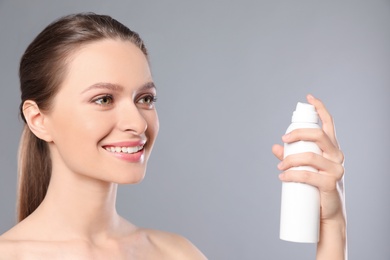 Young woman with bottle of thermal water on grey background. Cosmetic product