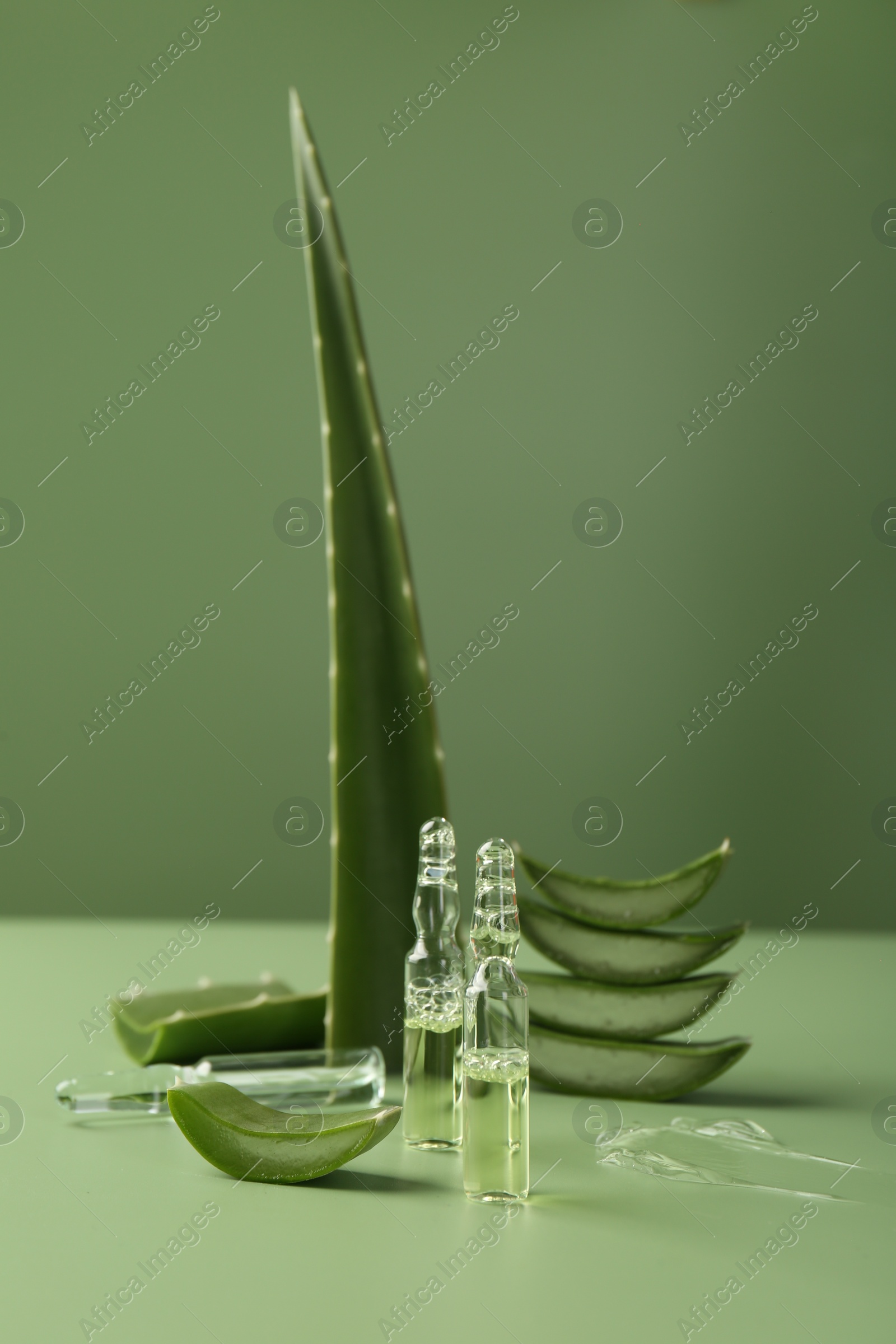 Photo of Skincare ampoules with extract of aloe vera and cut green leaves on color background