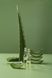 Photo of Skincare ampoules with extract of aloe vera and cut green leaves on color background