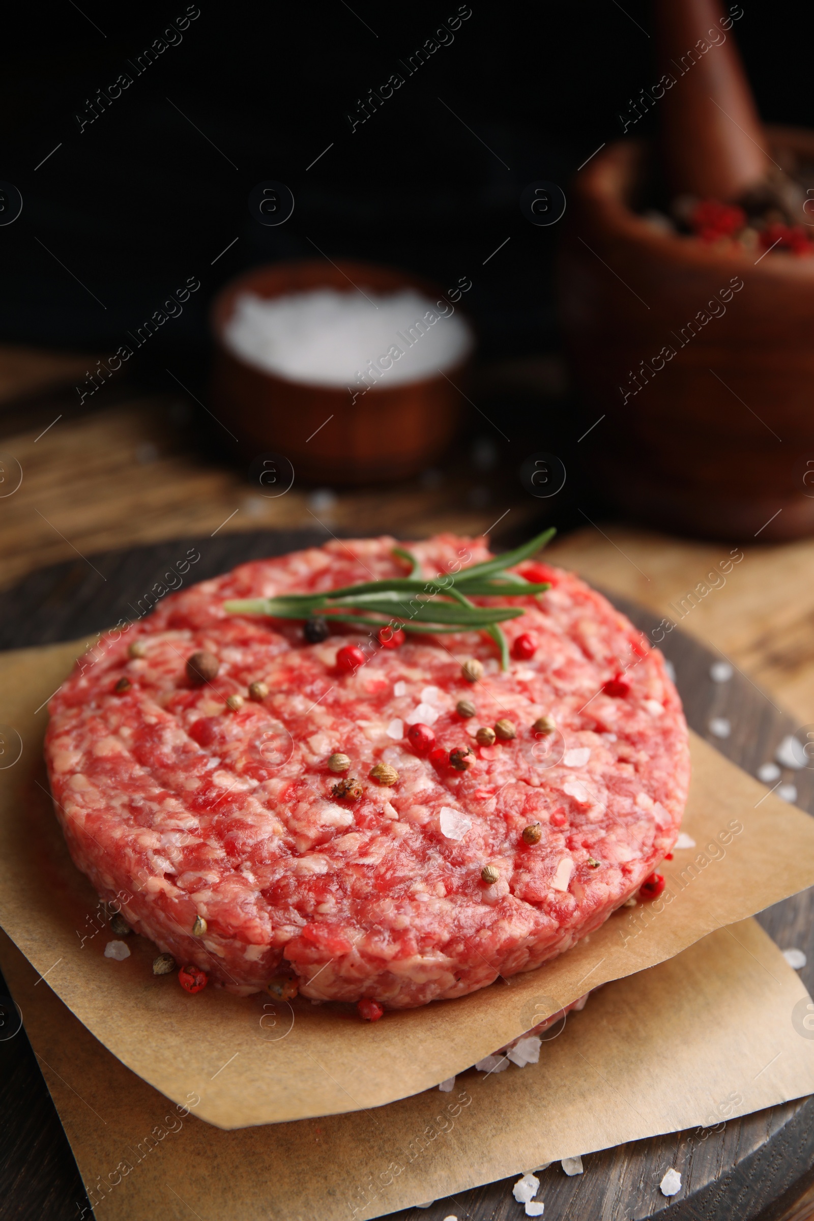 Photo of Raw hamburger patties with rosemary and spices on wooden board, closeup