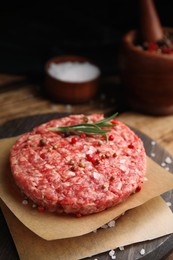 Photo of Raw hamburger patties with rosemary and spices on wooden board, closeup