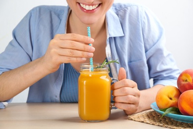 Woman with natural peach juice at wooden table, closeup