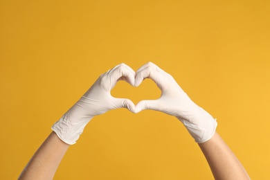 Photo of Doctor in medical gloves showing heart with hands on yellow background, closeup