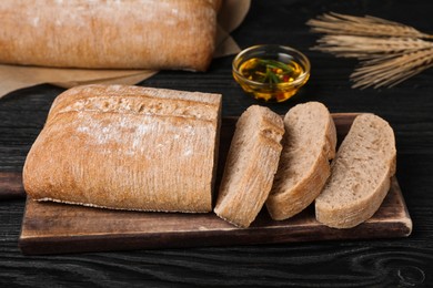 Cut delicious ciabatta on black wooden table