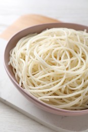 Bowl of tasty cooked rice noodles on white wooden table, closeup