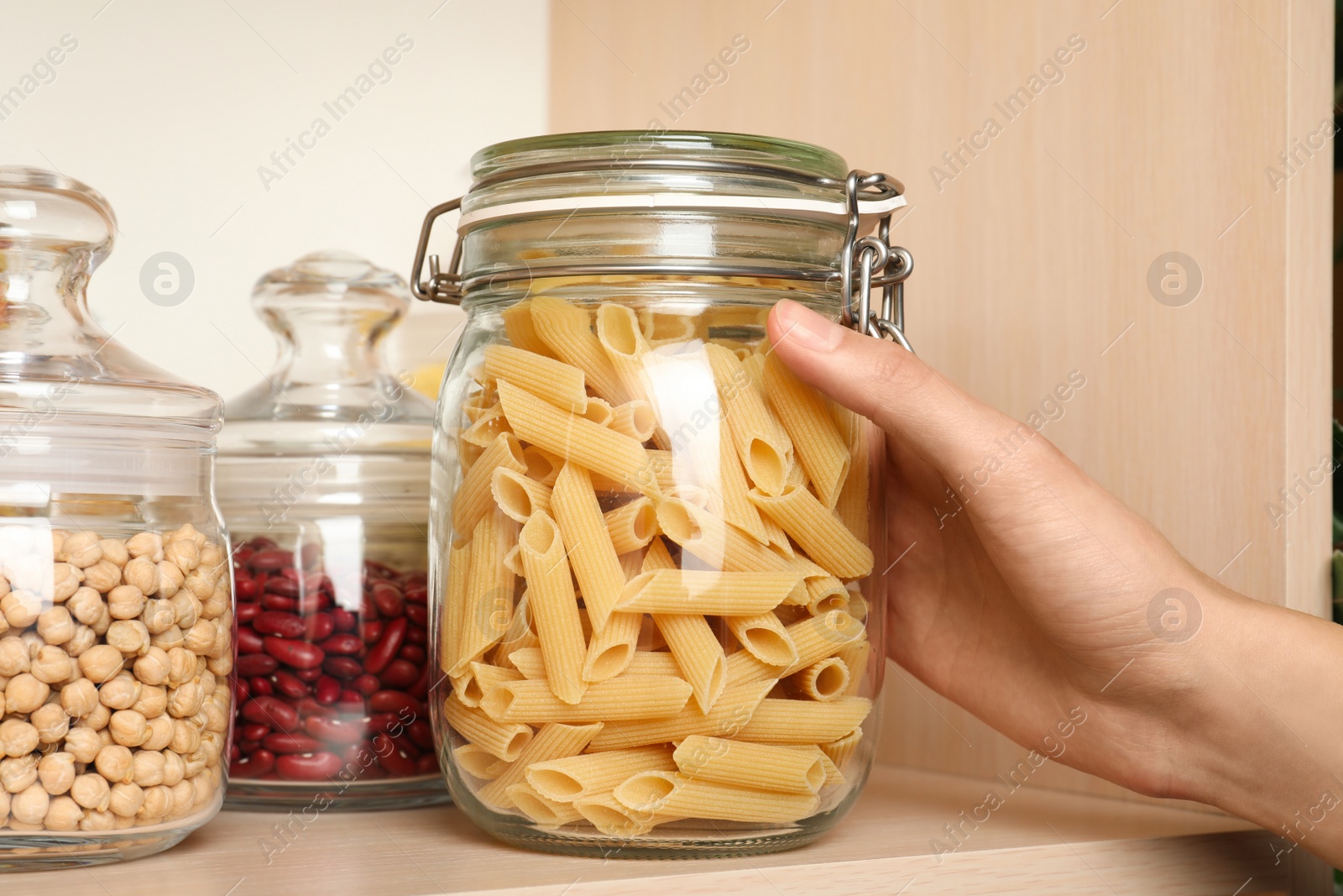 Photo of Woman taking jar of pasta from wooden shelf, closeup