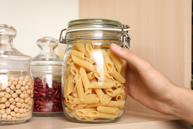 Woman taking jar of pasta from wooden shelf, closeup