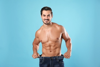 Young man with slim body in old big size jeans on light blue background