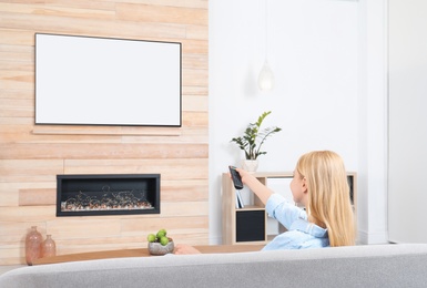 Photo of Woman watching TV on sofa in living room with decorative fireplace