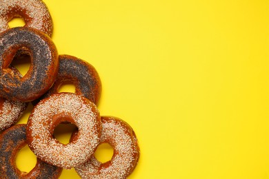 Many delicious fresh bagels on yellow background, flat lay. Space for text