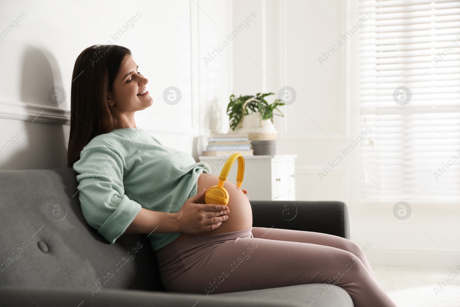 Photo of Beautiful pregnant woman with headphones on her belly at home