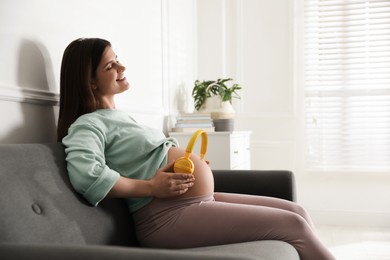 Photo of Beautiful pregnant woman with headphones on her belly at home