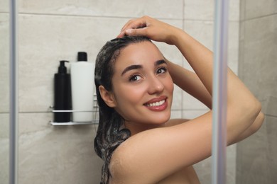 Beautiful happy woman washing hair with shampoo in shower