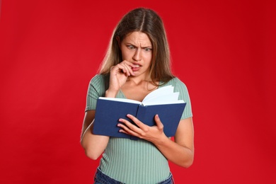 Beautiful young woman reading book on red background