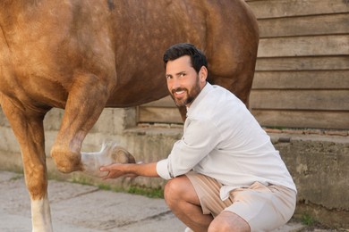Photo of Man examining horse leg outdoors. Pet care