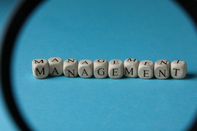 Photo of Word Management made of wooden cubes on light blue background, view through magnifying glass