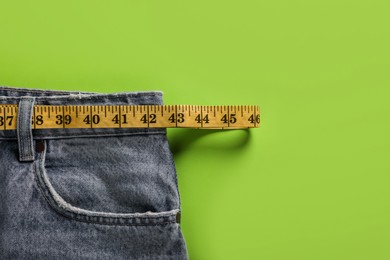 Photo of Jeans and measuring tape on green background, top view with space for text. Weight loss concept