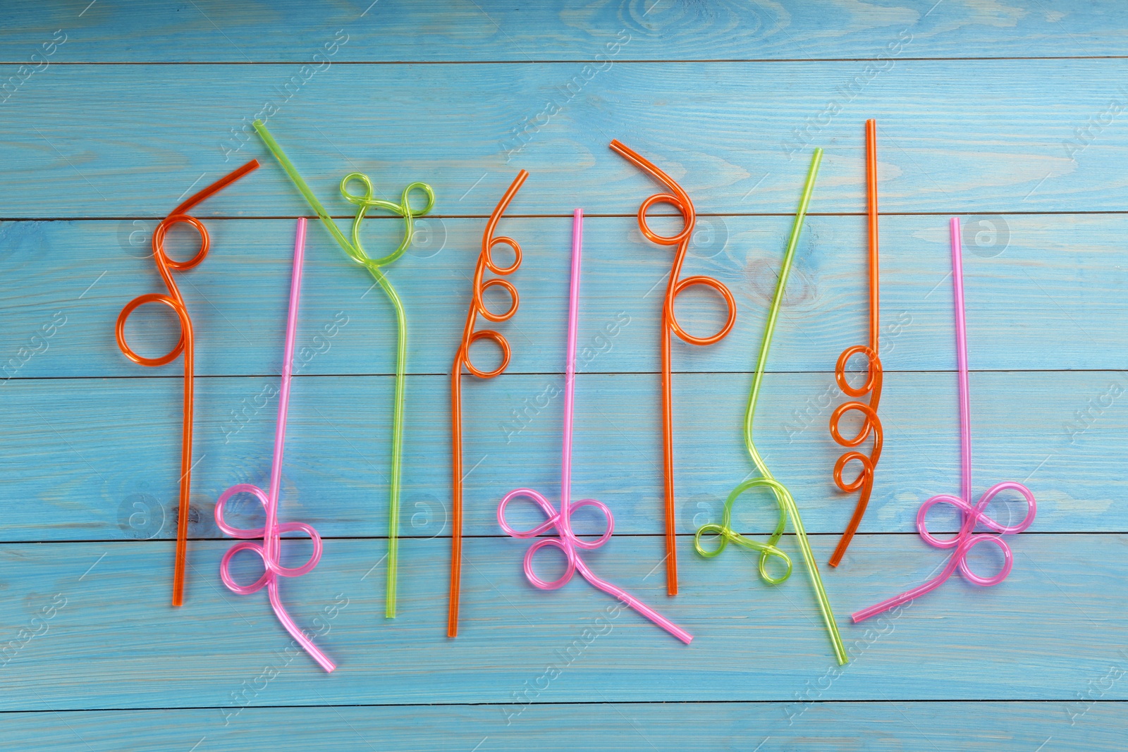 Photo of Colorful plastic drinking straws on light blue wooden table, flat lay