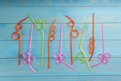 Colorful plastic drinking straws on light blue wooden table, flat lay