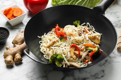 Stir fried noodles with chicken and vegetables in wok on white marble table