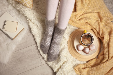 Photo of Woman and cup of hot winter drink on floor at home, above view