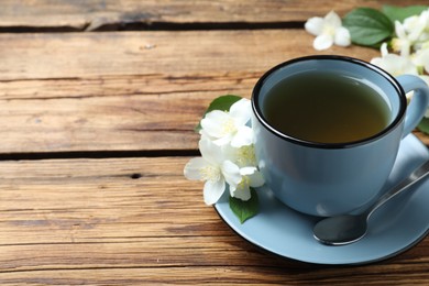 Photo of Cup of tea and fresh jasmine flowers on wooden table. Space for text
