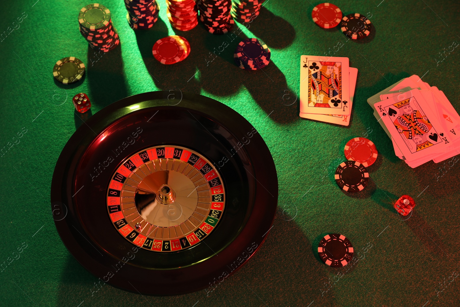 Photo of Roulette wheel with ball, playing cards and chips on green table, above view. Casino game