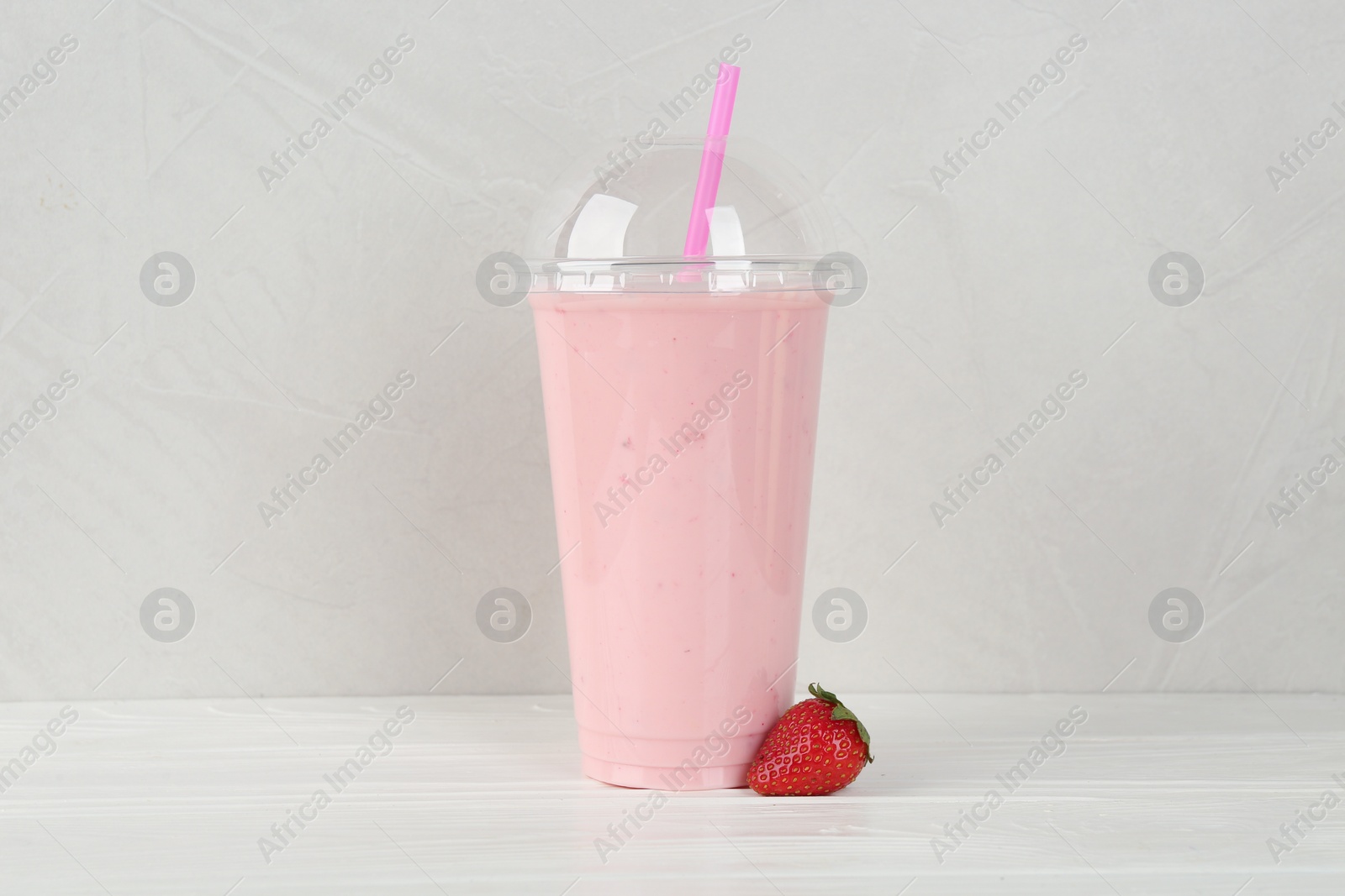 Photo of Plastic cup of tasty smoothie and fresh strawberry on white wooden table