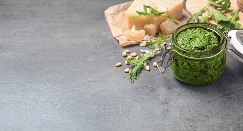 Jar of arugula pesto and ingredients on grey table, space for text. Banner design 