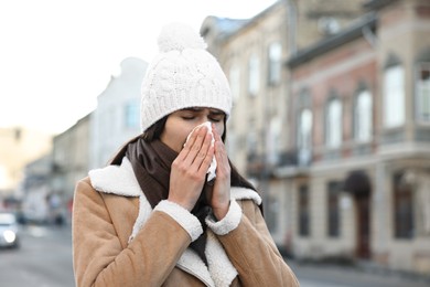 Woman with tissue blowing runny nose outdoors. Cold symptom